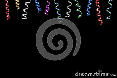 Horizontal image with multi coloured rolls curly ribons hanging from the top on black bacgroung Stock Photo
