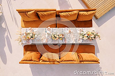 Festive long table with flowers near brown sofas. Top view Stock Photo