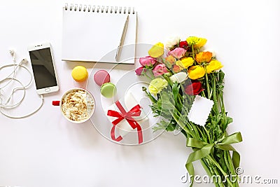 Festive morning concept buttercup flowers bouquet, gift box, cup of cappuccino, makarons cake, mobile, clean notebook, pen on the Stock Photo