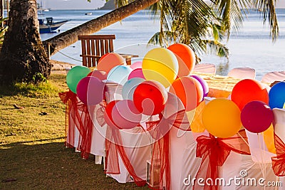 Festive table with colorful balloons on beach background with palm tree and boat. Happy birthday celebration concept. Stock Photo