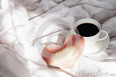 Festive Valentine's morning in bed. Handmade Valentine card and coffee cup on rumpled bedding Stock Photo