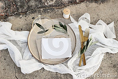 Festive wedding summer table setting. Golden cutlery, olive branch, glass of wine and envelope on porcelain dinner plate Stock Photo