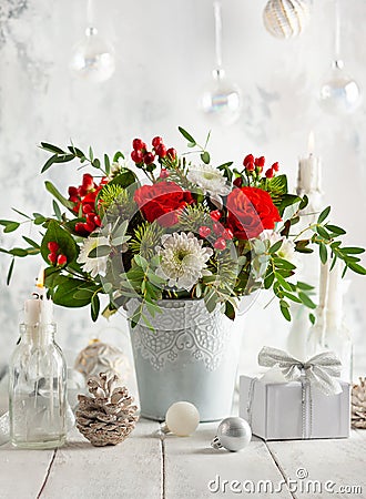 Festive winter flower arrangement with red roses, white chrysanthemum and berries in vase on table decorated for holiday. Stock Photo