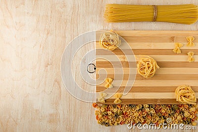 Fettuccine and Farfalle are laid out on a bamboo cutting Board and with other macaroni on a wooden background Stock Photo