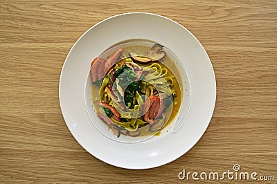 Fettuccine pasta in tasty broth fresh green wilted spinach and slices of smoked duck Stock Photo