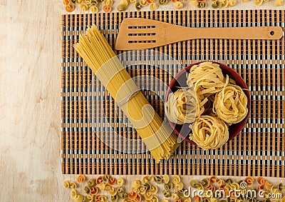 Fettuccine in a red Cup and spaghetti on a bamboo Mat laid out on a wooden background Stock Photo