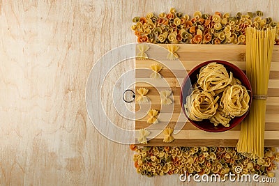 Fettuccine in a red Cup, spaghetti and Farfalle spread out on a bamboo cutting Board Stock Photo