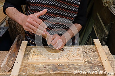 Fez, Morocco - close-up of male woodcarver hands with a chisel carving a block of wood. Woodworker at a woodshop in Fes el Bali. Editorial Stock Photo