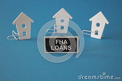 FHA mortgage loans symbol. Wooden houses sits next to a wooden black board with the word FHA loans. Beautiful blue background. Stock Photo