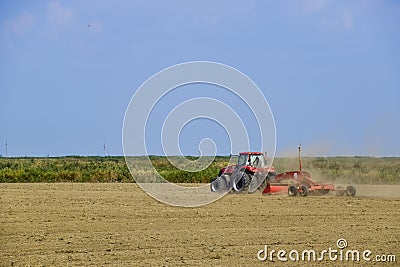 Tractor with a grader aligns the soil on the field. The tractor raised dust. Editorial Stock Photo