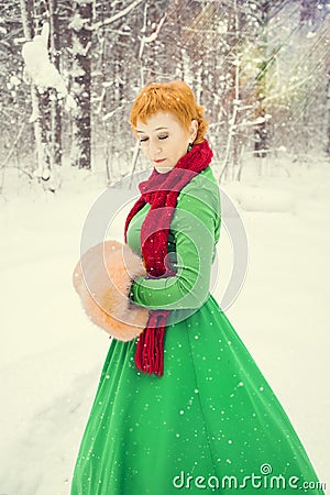 Fiery red-haired woman in a ball green dress with a red leather belt in the costume of dwarf assistant Santa Claus in the winter f Stock Photo