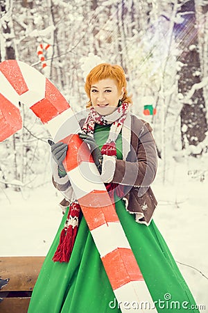 Fiery red-haired woman in a ball green dress with a red leather belt in the costume of dwarf assistant Santa Claus in Stock Photo