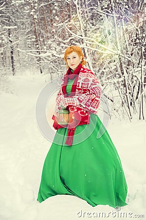 Fiery red-haired woman in a ball green dress with a red leather belt in the costume of dwarf assistant Santa Claus in the winter f Stock Photo