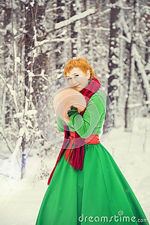 Fiery red-haired woman in a ball green dress with a red leather belt in the costume of dwarf assistant Santa Claus in the winter f Stock Photo