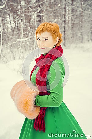 Fiery red-haired woman in a ball green dress with a red leather belt in the costume of dwarf assistant Santa Claus in the winter f Stock Photo