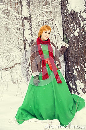 Fiery red-haired woman in a ball green dress with a red leather belt in the costume of dwarf assistant Santa Claus in the winter f Stock Photo