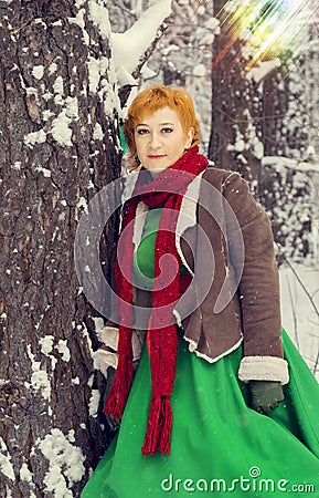 Fiery red-haired woman in a ball green dress with a red leather belt in the costume of dwarf assistant Santa Claus in the winter f Stock Photo