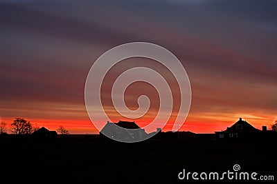 Fiery sky over silhouettes of farmhouses Stock Photo