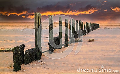 Fiery sunset sky over old water breaker, groyne on a wet sandy b Stock Photo