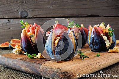 Fig appetizers with blue cheese, prosciutto and honey on a wood serving board Stock Photo