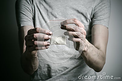 The fight against drugs and drug addiction topic: addict holding package of cocaine in a gray T-shirt on a dark background Stock Photo