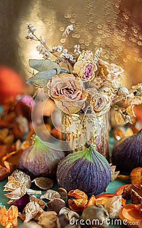 Figs and dry rose flowers in a small vase. Autumn composition and beautiful glowing bokeh on a blurred background of Stock Photo
