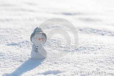 Figure of little cute snowman in a knitted hat and scarf on on snowy field in a sunny winter day. Stock Photo