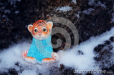 A figurine of a toy tiger cub on the snow against a background of tree bark. Stock Photo