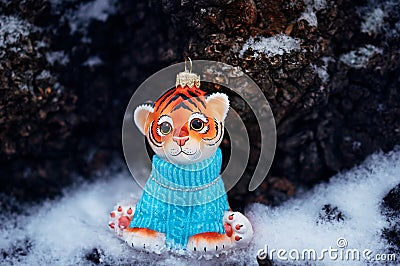 A figurine of a toy tiger cub on the snow against a background of tree bark. Stock Photo