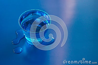 Filled blue glass of water on blue neon background with spilled water on it Stock Photo