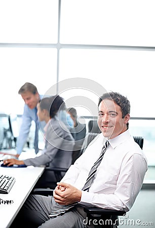 Filled with the confidence it takes to succeed. Positive businessman sitting at his desk with his colleagues working in Stock Photo