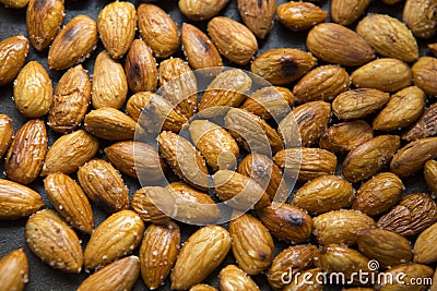 Filled frame background wallpaper shot of a bunch of crunchy roasted almonds with sea salt on a black background Stock Photo