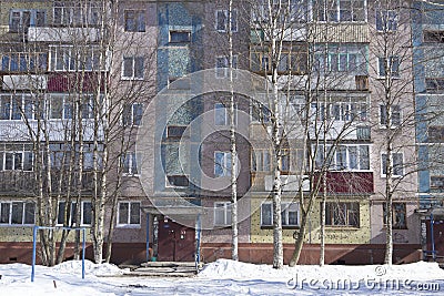 Filled frame full screen shot of an old ugly colorful facade of a soviet block house with windows, balconies and naked birches and Stock Photo