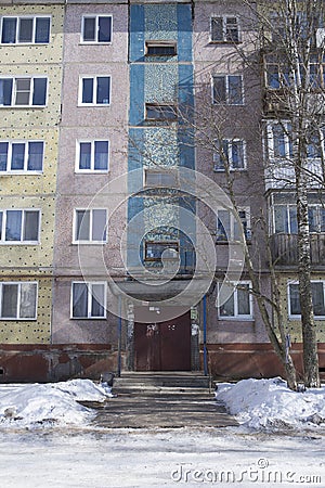 Filled frame full screen shot of an old ugly colorful facade of a soviet block house with windows, balconies and naked birches and Stock Photo