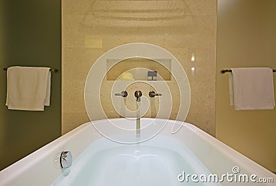 Filled white bathtub with brass tap mounted on the marble wall and shower screens on both sides Stock Photo