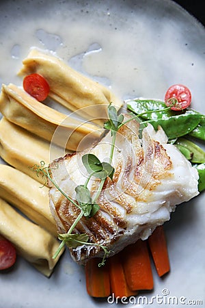 Fillet of cod with dumplings, carrots, green sweet pea and tomatoes at vegetarian restaurant Stock Photo