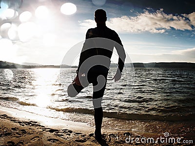 Film grain. Silhouette of person in sportswear and short hair on beach seeing into morning Sun above sea Stock Photo