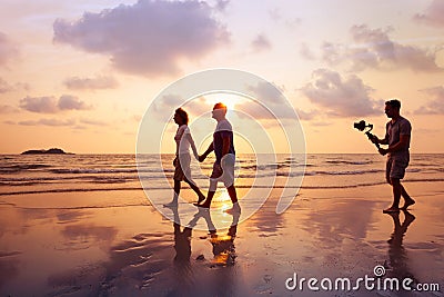 Filmmaker filming video of couple with camera stabilizer on the beach Stock Photo