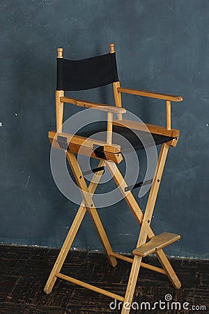 A filmmakers chair with wooden legs and a black seat stands against a gray-blue wall Stock Photo