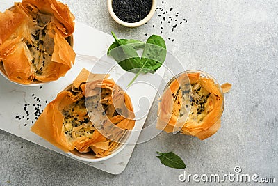 Filo pies with soft feta cheese and spinach in ceramic molds on old grey table background. Filo portions pies. Small Baked Stock Photo