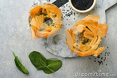 Filo pies with soft feta cheese and spinach in ceramic molds on old grey table background. Filo portions pies. Small Baked Stock Photo