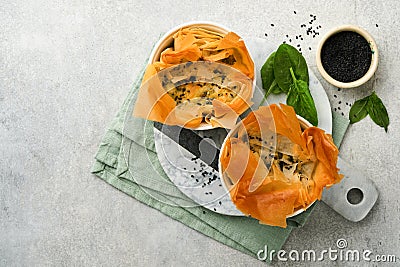 Filo pies with soft feta cheese and spinach in ceramic molds on old grey table background. Filo portions pies. Small Baked Stock Photo