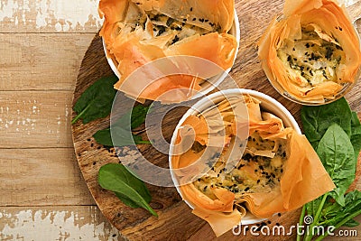 Filo pies with soft feta cheese and spinach in ceramic molds on old wooden table background. Filo portions pies. Small Baked Stock Photo