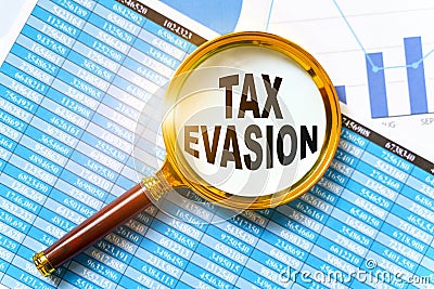 Financial reports, charts and a magnifying glass are on the table. Inside the magnifier there is an inscription - TAX EVASION Stock Photo