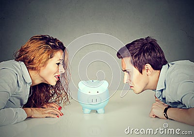 Finances in divorce concept. Wife and husband can not make settlement looking at piggy bank sitting at table looking at each other Stock Photo