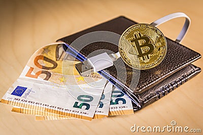 Financial concept with golden Bitcoin over a wallet with Euro bills and USB cable Stock Photo