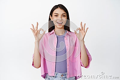 Fine, no problem. Smiling brunette woman shows okay, zero gesture, recommending something good, standing over white Stock Photo