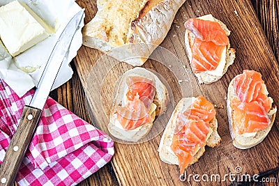 Finger food. Appetizer canapes sandwiches with baguette, salmon and butter on rustic wooden board over wood background. Top view, Stock Photo