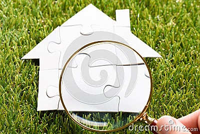 Finger Holding Magnifying Glass Over Puzzle House Stock Photo