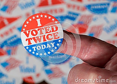 Finger with I Voted Twice sticker in front of many election voting badges to illustrate voter fraud Stock Photo